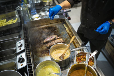 Man sprinkling salt on meat while standing by gas stove at commercial kitchen