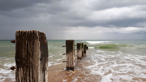 Wooden posts on sea against sky