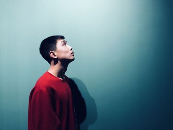 Side view of young man standing against blue background