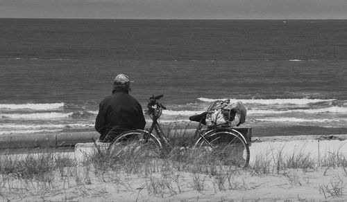 Rear view of man sitting at beach against sky