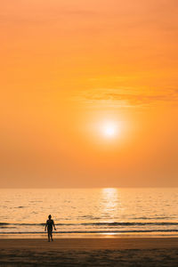 Silhouette man walking at beach against orange sky