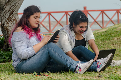 Full length of friends using laptop and book at park