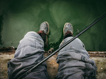 Low section of man sitting with fishing rod by lake