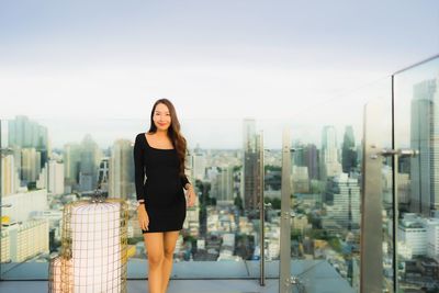 Portrait of young woman in city against sky