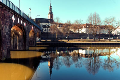 Bridge over river by buildings against sky