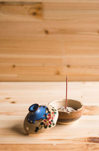 Burning incense stick on container against wooden wall