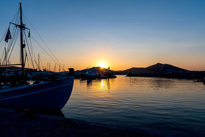 Sailboats moored on sea against sky during sunset