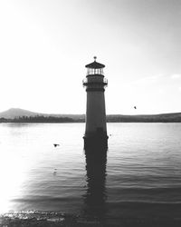 Lighthouse by sea against clear sky