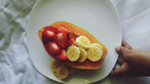 Cropped hand of person holding fresh fruits in plate on bed