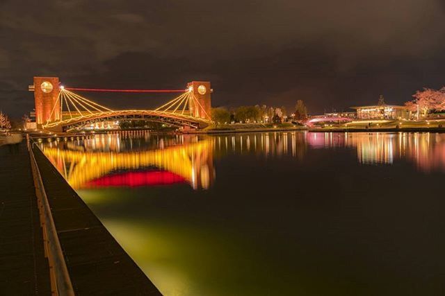 illuminated, water, architecture, built structure, bridge - man made structure, connection, night, river, suspension bridge, engineering, waterfront, reflection, bridge, city, travel destinations, transportation, building exterior, sky, sea, famous place