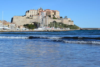 Buildings by sea against clear blue sky