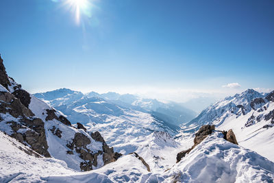 Sun shining on snowy mountain range against sky