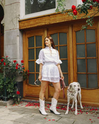 Portrait of young woman with dog standing against wall