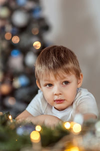 Portrait of cute boy siting at home against christmas tree