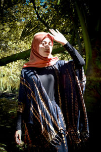 Portrait of woman standing by tree against plants