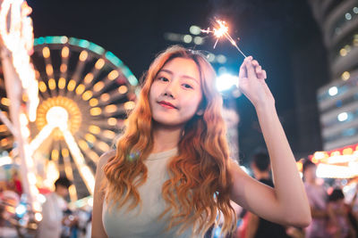 Portrait of young woman holding illuminated sparklers at night