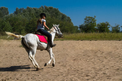 Full length of young woman riding horse on field