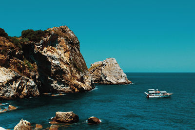 Rocks by sea against clear blue sky