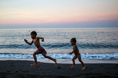 Full length of men on beach against sky during sunset