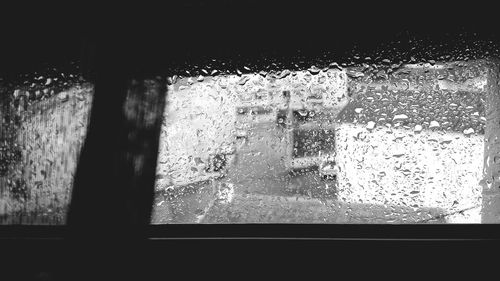 Close-up of wet glass window against sky