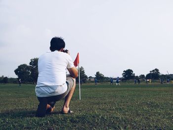 Man photographing while crouching on field against clear sky