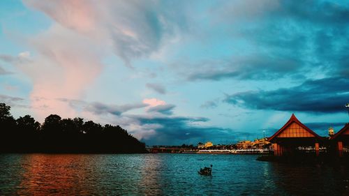 Scenic view of lake by buildings against sky during sunset