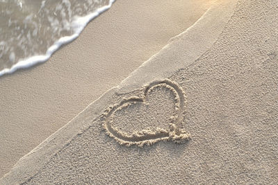 Hand written heart shape in the sand on the beach with beautiful warm sunlight in the morning. 