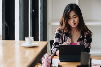 Young woman using phone while sitting on table