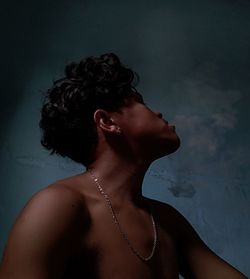 Shirtless young man smoking while sitting against wall