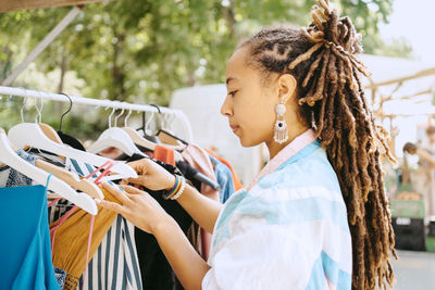 Side view of female customer with dreadlocks buying dress at flea market