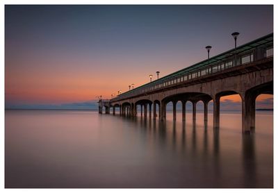 Bridge over sea against sky during sunset