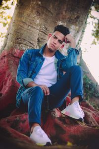 Low angle portrait of young man sitting on tree trunk