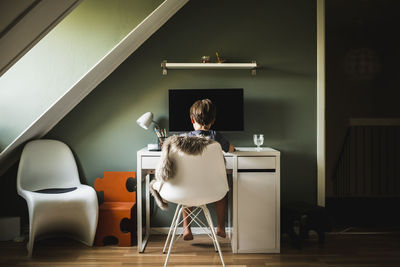 Rear view of boy sitting in front of computer at desk
