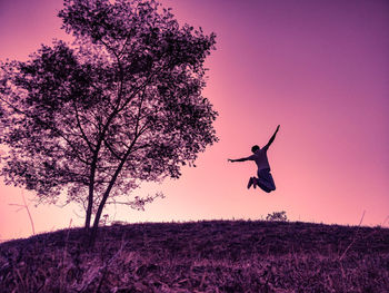 Low angle view of man jumping on field against sky during sunset