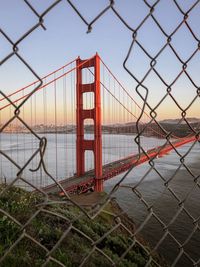 Bridge over sea against sky seen through chainlink fence