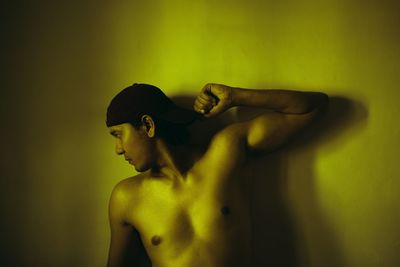 Side view of shirtless man looking away against wall