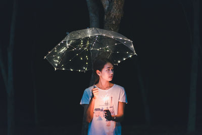 Woman with sparkler holding illuminated umbrella at night