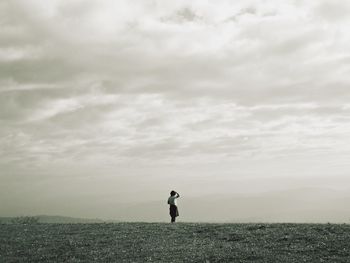 Person standing on hill against cloudy sky