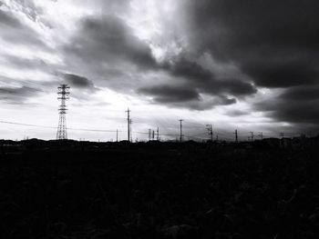 Electricity pylon on field against cloudy sky