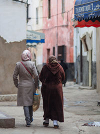 Rear view of women walking on street against buildings