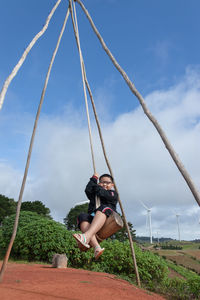 Boy enjoying swing against sky