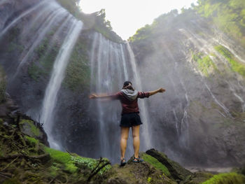 Blurred motion of woman outstretching in front of waterfall