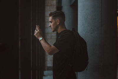 Side view of young man photographing while standing against wall