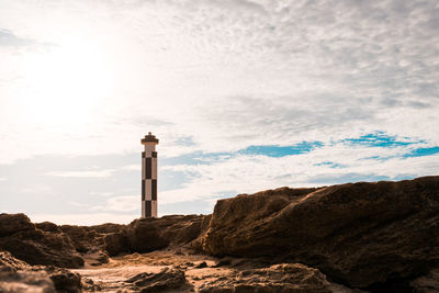 Lighthouse on rock amidst buildings against sky