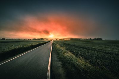 Road amidst field against sky during sunset