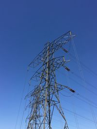 Low angle view of electricity pylon against clear blue sky