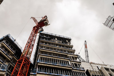 Low angle view of crane by building against sky