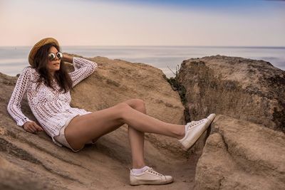 Woman sitting on rock at beach against sky