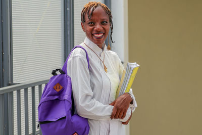 A pretty black female african student carrying books and a school bag and smiling