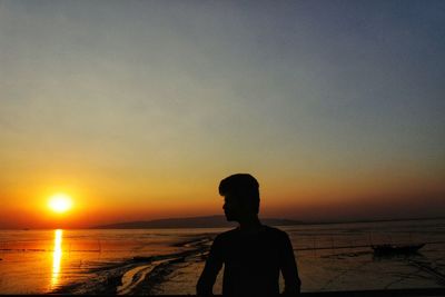 Silhouette woman standing on beach against clear sky during sunset